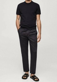 Zwarte gebreide T-shirt met korte mouwen, gecombineerd met donkere broeken met een slim fit en elastische taille, gedragen met zwarte slip-on sandalen.