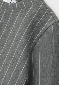 Maglione grigio con strisce verticali bianche, con collo a costine e texture liscia. I dettagli includono cuciture sulla spalla.