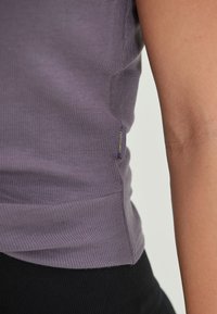 Lilla ribbet tanktop med en tætsiddende design, der har et sidelabel. Stoffet har en blød tekstur, der står i kontrast til sorte tætsiddende bukser.