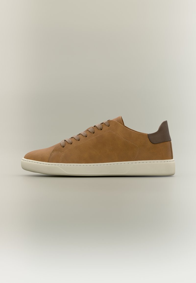 Baskets basses en cuir marron avec semelle beige et lacets assortis, présentant une languette de talon marron plus foncé sur un fond neutre.