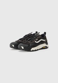 Black athletic sneakers with textured fabric, rubber sole, lace-up design, contrasting white and beige accents, and a Vibram logo.