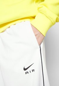 Vita idrottsbyxor med svarta detaljer och "NIKE AIR" logotyp, tillsammans med en klar gul sweatshirt med ribbade muddar.