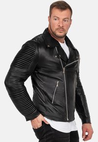 Zwarte leren motorjack met ribbeltextuur op de mouwen, asymmetrische frontrits en zilverkleurige hardware accenten.