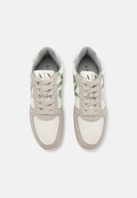 Hellgraue und weiße Sneaker mit Netz- und Ledertexturen, die grüne Akzente und flache Schnürsenkel aufweisen. Branding auf der Zunge sichtbar.