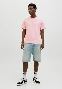 Lichtroze katoenen T-shirt met een licht gestructureerde afwerking, gecombineerd met blauwe denim shorts. Zwart-witte sneakers met gestreepte sokken maken de look compleet.