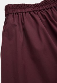 Bordeaux korte broek met een elastische tailleband en een gladde, geweven textuur. Beschikt over een ontspannen pasvorm en zijzakken voor functionaliteit.