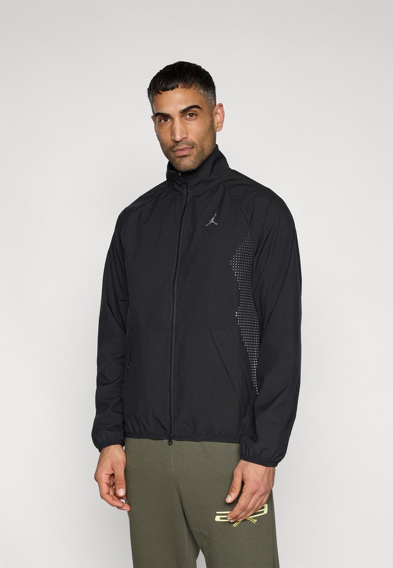 Μαύρο αθλητικό μπουφάν με ψηλό γιακά, ολόκληρο φερμουάρ και πουά σχέδιο στη μία πλευρά. Διαθέτει ελαστικά μανίκια και τσέπες.