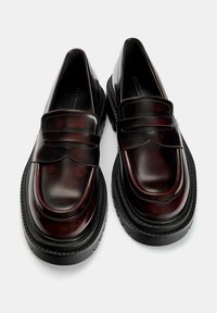 Pair of dark brown leather loafers with thick black rubber soles, rounded toes, and penny strap detail on a light background.
