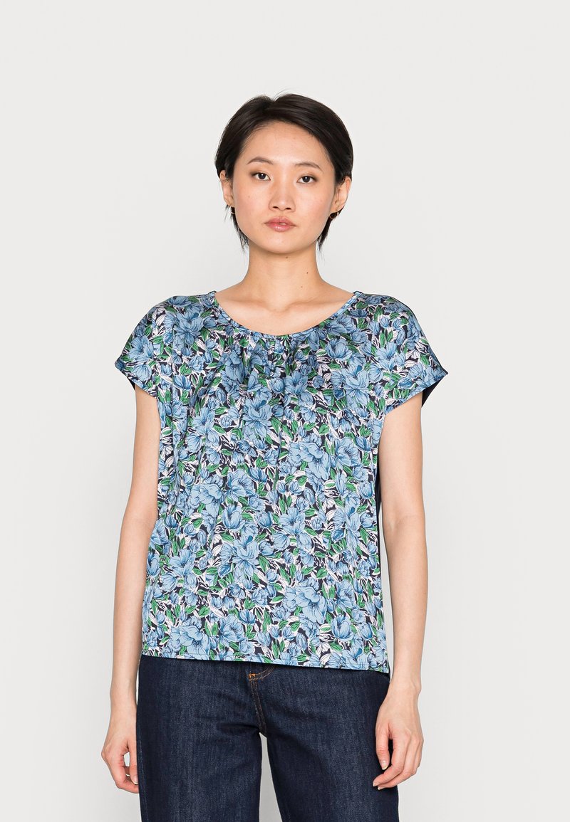 Top floral de manga curta em azul claro com detalhes em verde e preto. Apresenta um decote redondo e leve pregueado na gola.