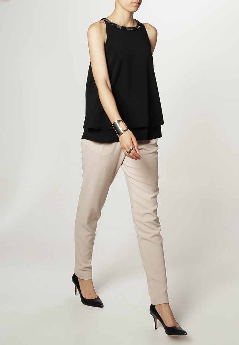 Svart ärmlös topp med ett lagerdesign och dekorerad halsringning, tillsammans med ljusbeige tapered byxor och svarta högklackade skor.