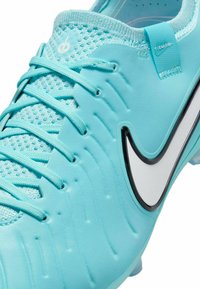 Botte de football turquoise avec empeigne texturée, fermeture à lacets et swoosh Nike noir. Présente un matériau doux et une forme moulée pour un soutien optimal.