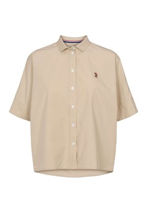 Bež kratka srajca s kratkimi rokavi in ovratnikom z gumbi. Vsebuje subtilen izvezen emblem na prsih in ukrivljen rob. Gladek tekstura tkanine.