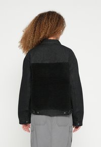 Fekete farmerruha kabát fekete bolyhos birkabőr hátpanelekkel, patentokkal az ujjvégeknél és kényelmes szabással.