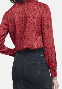 Rode bloempatronde blouse met lange mouwen, zijdezachte structuur, geplooide details, gecombineerd met een zwarte high-waisted spijkerrok met zakken.
