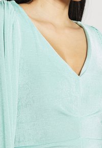 Robe vert menthe avec un décolleté en V et un tissu texturé, dotée de manches drapées et de détails de couture.