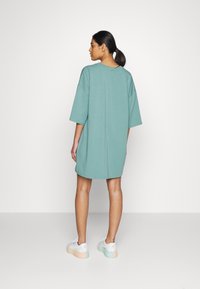 Vestido t-shirt oversized em azul claro, com mangas curtas, decote redondo e um corte descontraído, combinado com ténis brancos com detalhes em tons pastel.