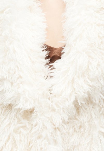 Puhast bela umetna krznena oblačila z globokim V-izrezom, ki ima mehko teksturo in spodnjo plast rjavega blaga.