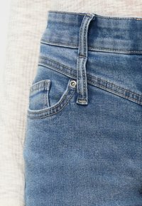 Φωτεινό γαλάζιο τζιν παντελόνι με ψηλή μέση, διαθέτοντας μπροστινή τσέπη, κούμπωμα με κουμπί και διακριτικές ραφές. Απαλή υφή.