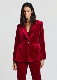Blazer en velours rouge avec un revers cranté, une fermeture à un bouton doré et deux poches avant. Texture lisse avec une silhouette ajustée.