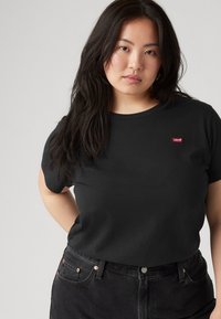 Black cotton t-shirt with short sleeves, featuring a small red Levi's logo on the chest. Paired with high-waisted black jeans.