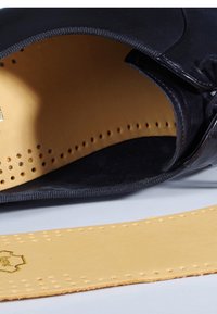 Black leather shoe interior with beige insole featuring perforations. Smooth texture, stitched edges, and a logo embossed on the insole.