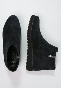 Botines de ante negro con cremallera lateral, detalles de brogue y suelas gruesas de goma con dibujo, mostrados desde vistas superiores y laterales.