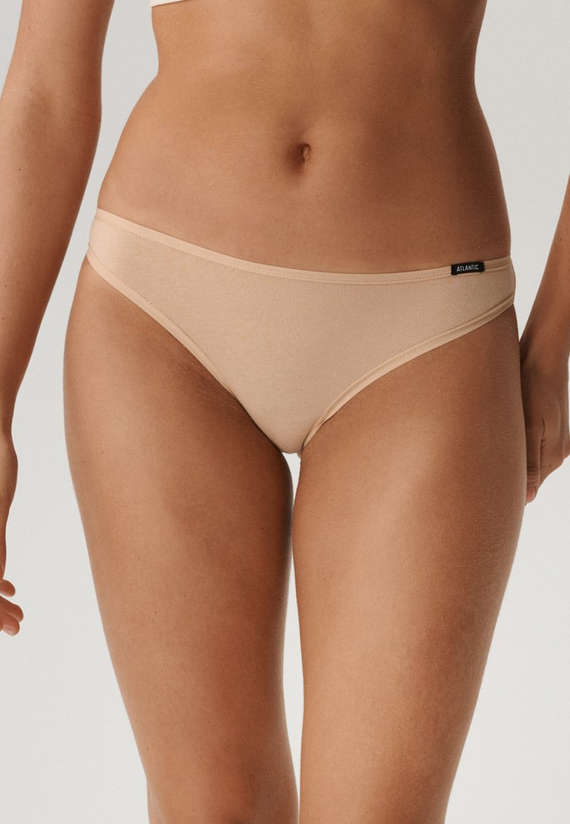 Beżowe majtki bikini z miękkiego materiału, charakteryzujące się niskim stanem i metką na pasie. Gładka tekstura z minimalnymi szwami.