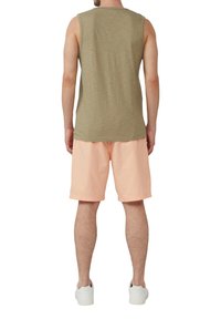 Maglietta senza maniche color verde oliva abbinata a pantaloni shorts rosa chiaro, caratterizzata da una vestibilità comoda e un design semplice. Indossata con scarpe da ginnastica bianche.