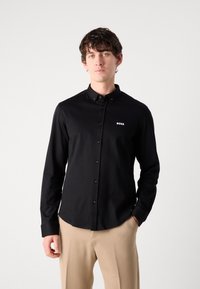 Zwarte overhemd met kraag, voorzien van een klein wit "BOSS" logo op de borst. Gladde textuur, getailleerd ontwerp en lange mouwen.