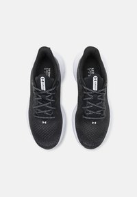 Zapatillas deportivas negras con parte superior de malla, suela blanca y cordones en contraste en blanco y negro. Presenta un logo en el lateral y en la lengüeta.