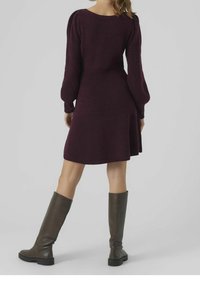 Burgundy stickad klänning med långa puffärmar, ovanför knäna, utsvängd nederkant och textilstruktur. Matcher med mörkbruna knähöga stövlar.