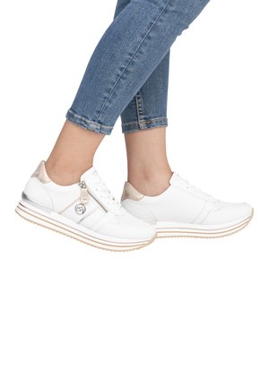 Weiße Sneakers mit metallischen Akzenten, strukturierten Paneelen, einem Reißverschluss und einer gepolsterten Sohle, kombiniert mit gerollten blauen Denim-Jeans.