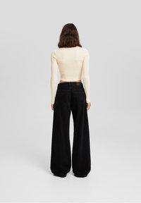 Top largo de manga larga de canalé en crema, combinado con pantalones negros de pierna ancha y cintura alta. El conjunto presenta telas suaves y una silueta ajustada.