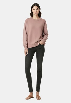 Maglione rosa lavorato a maglia con scollo rotondo, polsini e orlo a costine; abbinato a jeans skinny scuri e sandali bassi marroni.