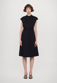 Mornarska haljina s ovratnikom, kratkim rukavima, dugmadi sprijeda, dva džepa na prsima, strukom s remenom i suknjom koja se širi. Glatka tekstura tkanine.