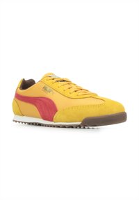 Sneakers Puma in suede giallo e materiale sintetico, con accenti rossi e suola marrone. Design con lacci e punta arrotondata.