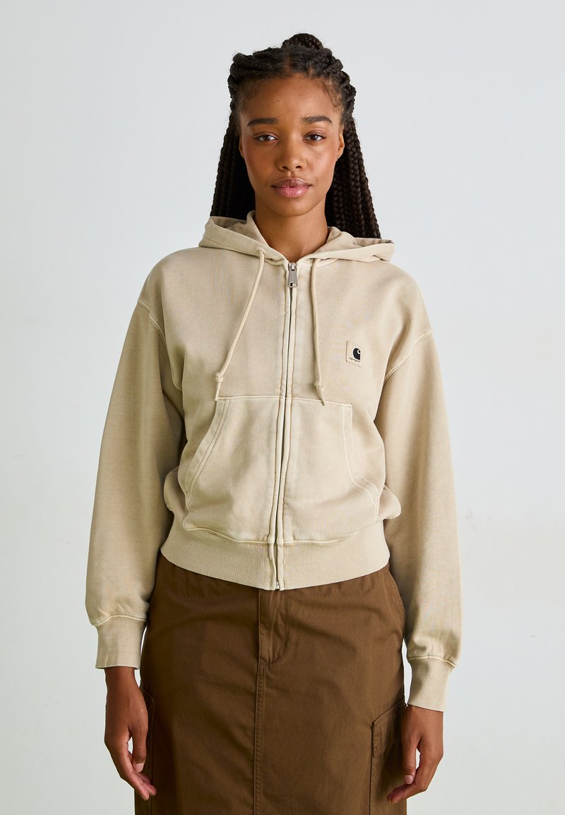 Gilet à capuche zippé beige en tissu doux, avec une poche avant, un cordon de serrage à la capuche et un logo brodé sur la poitrine gauche.
