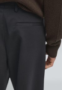 Mørkegrå skræddersyede bukser med en glat tekstur, forsynet med en skjult baglomme, parret med en struktureret brun sweater.