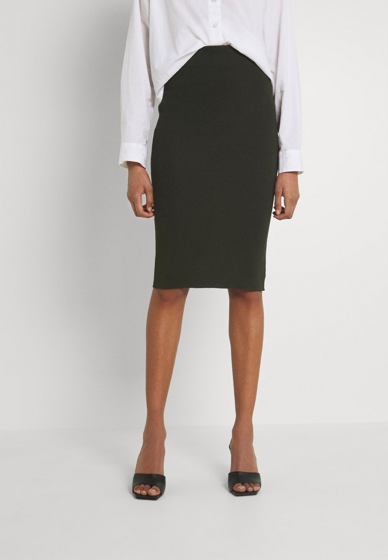 Svart knälång pennkjol med en mjuk textur, hög midja och tillsammans med en lös sittande vit skjorta med knappar samt svarta sandaletter med öppen tå.