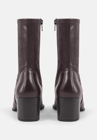 Botas de tobillo de cuero morado con punta cuadrada, cierre de cremallera y un tacón grueso. Textura suave con detalles de costura sutiles en las costuras.