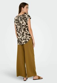 Top a maniche corte in stampa animale beige e marrone, abbinato a pantaloni larghi verde oliva, entrambi con texture lisce.