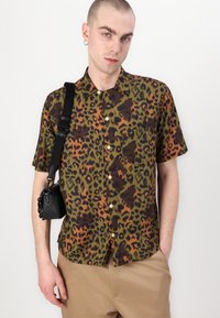 Camisa de botones de manga corta con un estampado de leopardo en verde, marrón y naranja, fabricada con tejido texturizado, y con un bolsillo en el pecho.