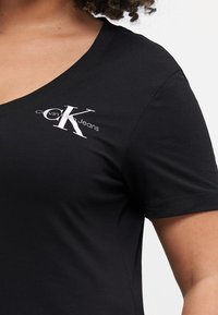 Juodas trumpas rankovėmis marškinėliai, pagaminti iš lygaus medvilnės, su giliu V formos iškirpimu. Puošia baltas Calvin Klein Jeans logotipas kairiajame krūtinės šone.