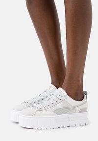Sneaker grigie chiare con tomaia testurizzata, lacci piatti, suola platform spessa e bianca, e accenti di logo discreti.