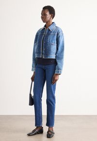 Giacca di jeans azzurro chiaro con colletto classico, tasche sul petto e chiusura a bottoni, abbinata a jeans skinny blu scuro e scarpe piatte nere.