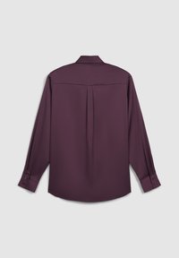 Chemise à manches longues en satin de couleur violet profond. Présente une coupe droite, des poignets boutonnés et un détail plissé au dos.
