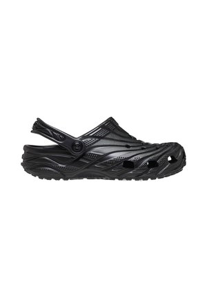 Sabot en caoutchouc noir avec trous de ventilation, semelle texturée et bride réglable au talon, vu de côté sur fond blanc.