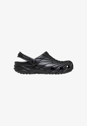 Zueco negro de goma con agujeros de ventilación, suela texturizada y correa ajustable en el talón, mostrado de perfil sobre fondo blanco.
