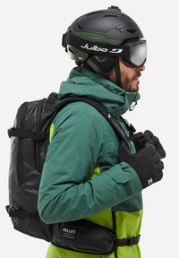 Czarny kask narciarski z lustrzanymi goglami, zielona kurtka w kratę, czarne rękawice i plecak w kolorze czarnym z wieloma kieszeniami. Teksturowane materiały i regulowane paski.