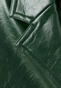 Materiale in pelle verde con una finitura testurizzata. Presenta bordi del colletto netti, cuciture visibili e una superficie liscia e lucida.